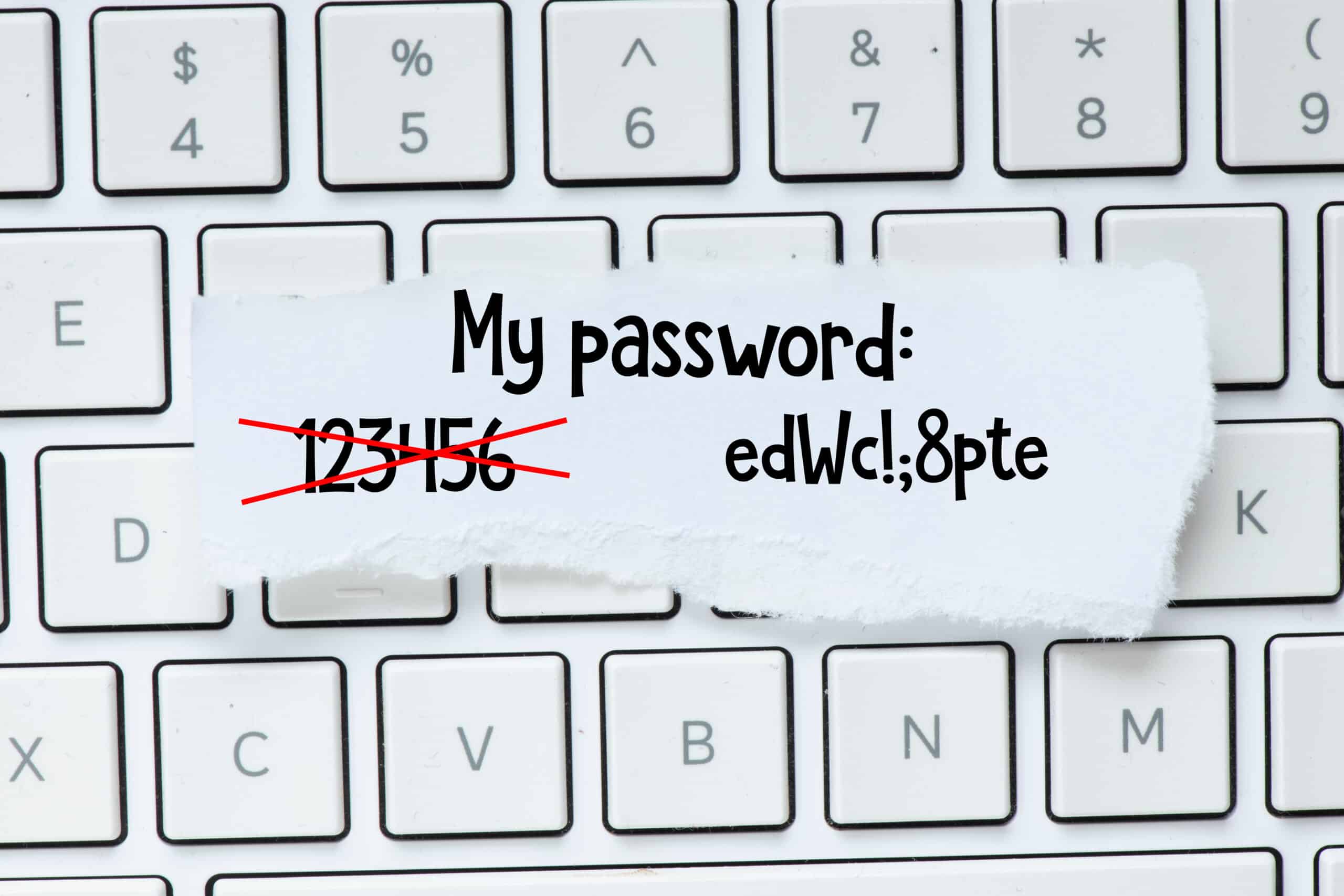 A handwritten note sits on a keyboard; the note changes a password from an embarrassingly weak one to a strong one.